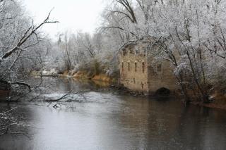 Archibald Flour Mill in the winter, from the Cannon River.  It is surrounded by frosted-over trees.